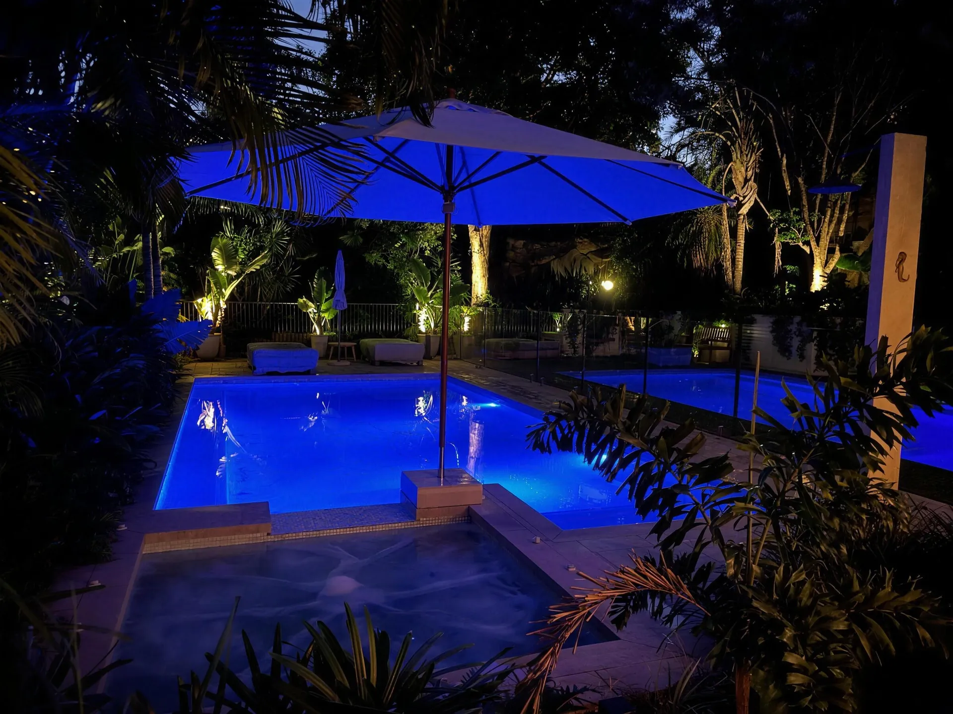 Bespoke pool lit at night with tropical landscaping